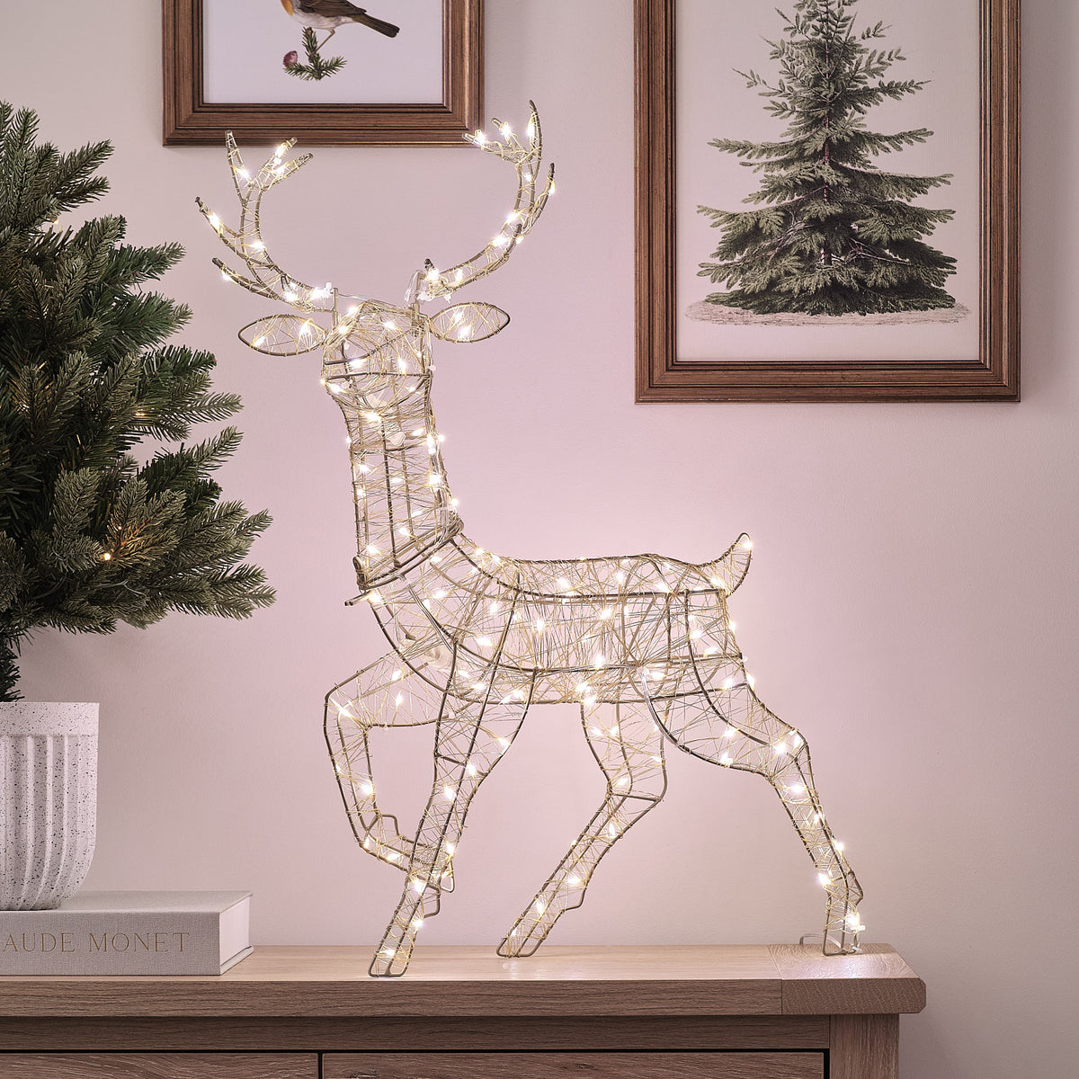 Goldenes LED-Rentier mit warmweißen Lichtern auf Sideboard vor Wand mit Bilderrahmen