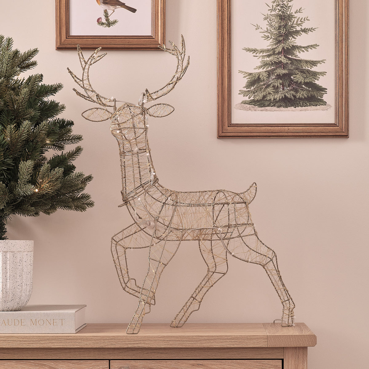 Goldene LED-Rentier-Hirschkuh ohne Beleuchtung auf Sideboard vor Wand mit Bildern