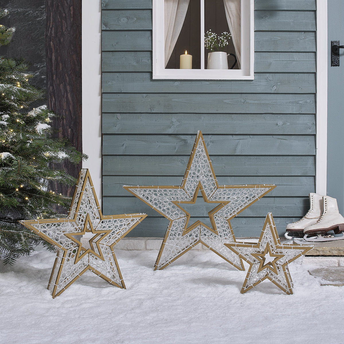 Drei unbeleuchtete goldene Sterne mit Acrylfüllung auf Schnee vor Hauswand mit Fenster