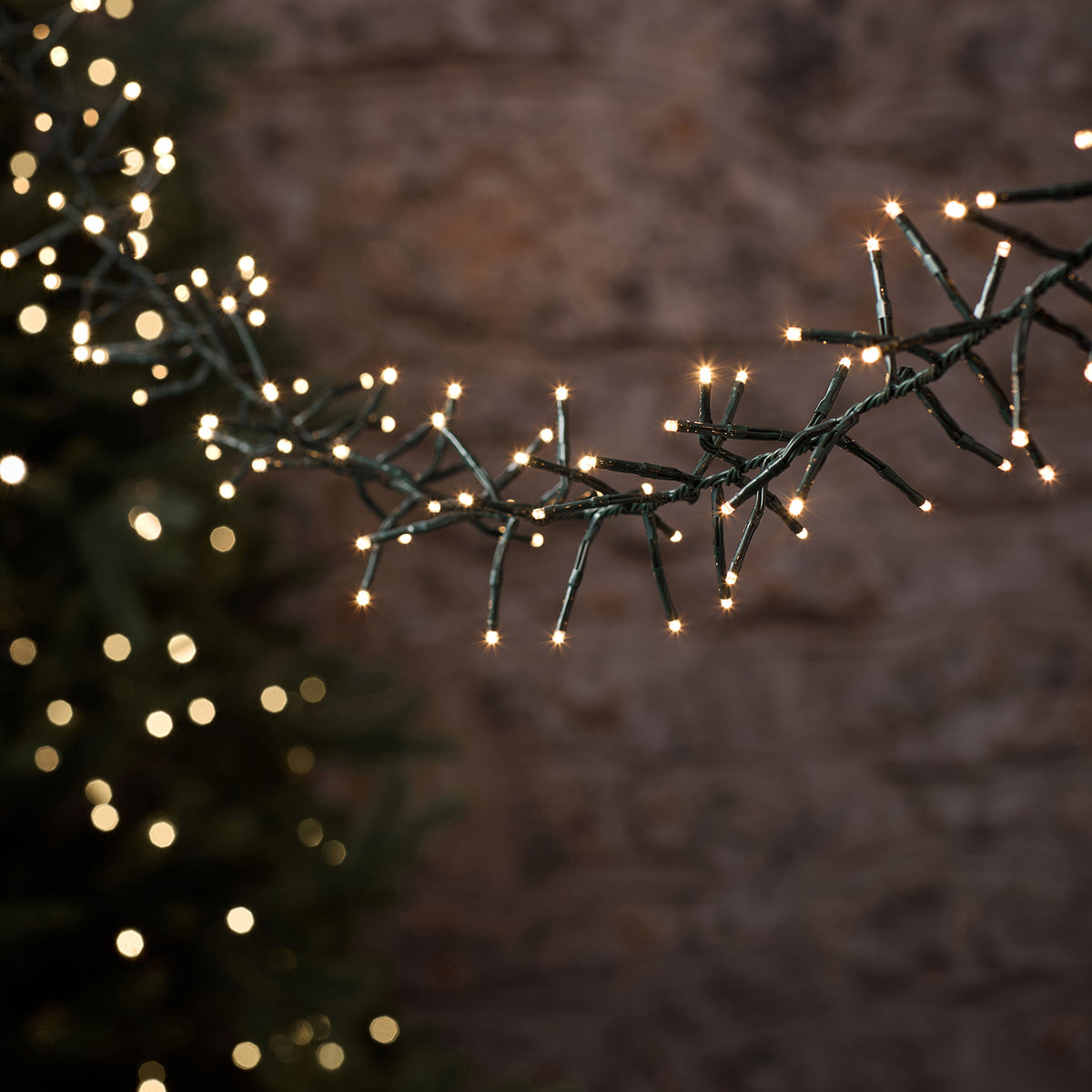Warmweiße LED-Cluster-Lichterkette mit dicht angeordneten LEDs an grünem Kabel im Dunkeln leuchtend