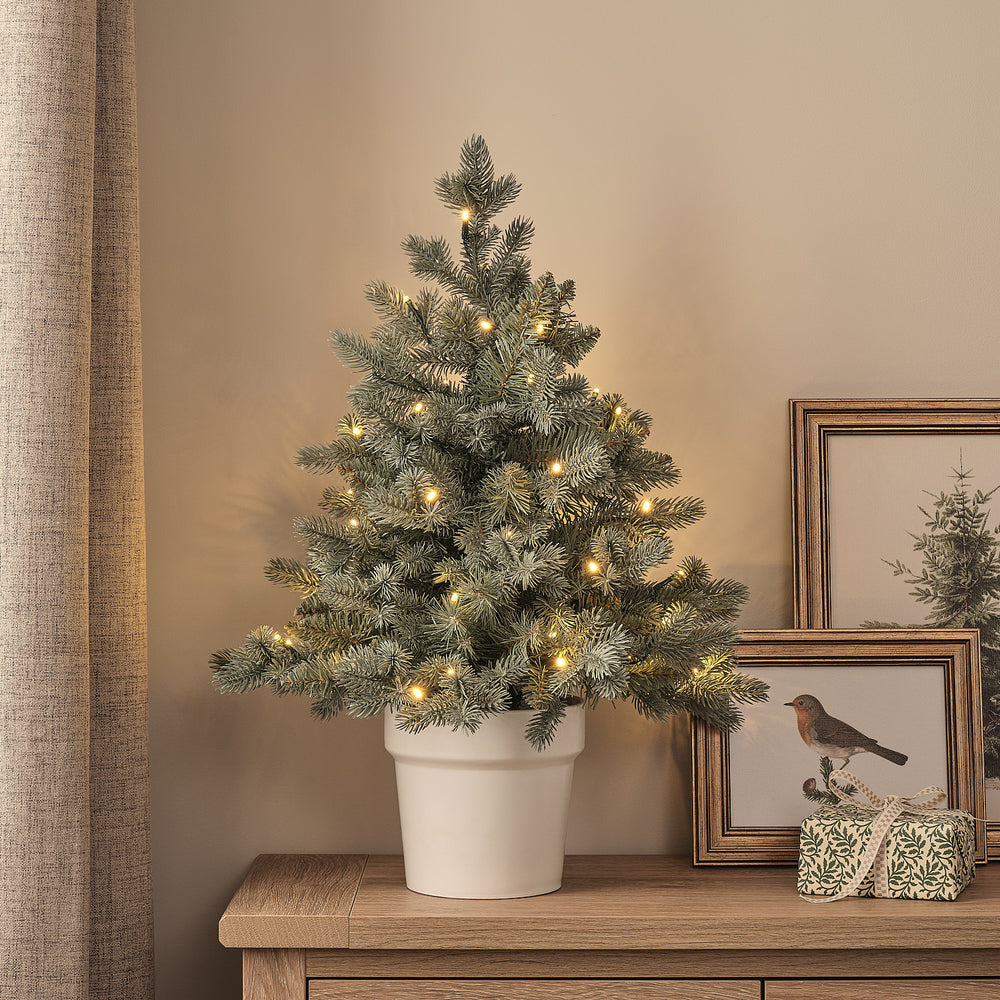 60cm künstlicher Douglasien-Weihnachtsbaum im weißen Topf mit warmweißen LED-Lichtern auf Holzkommode