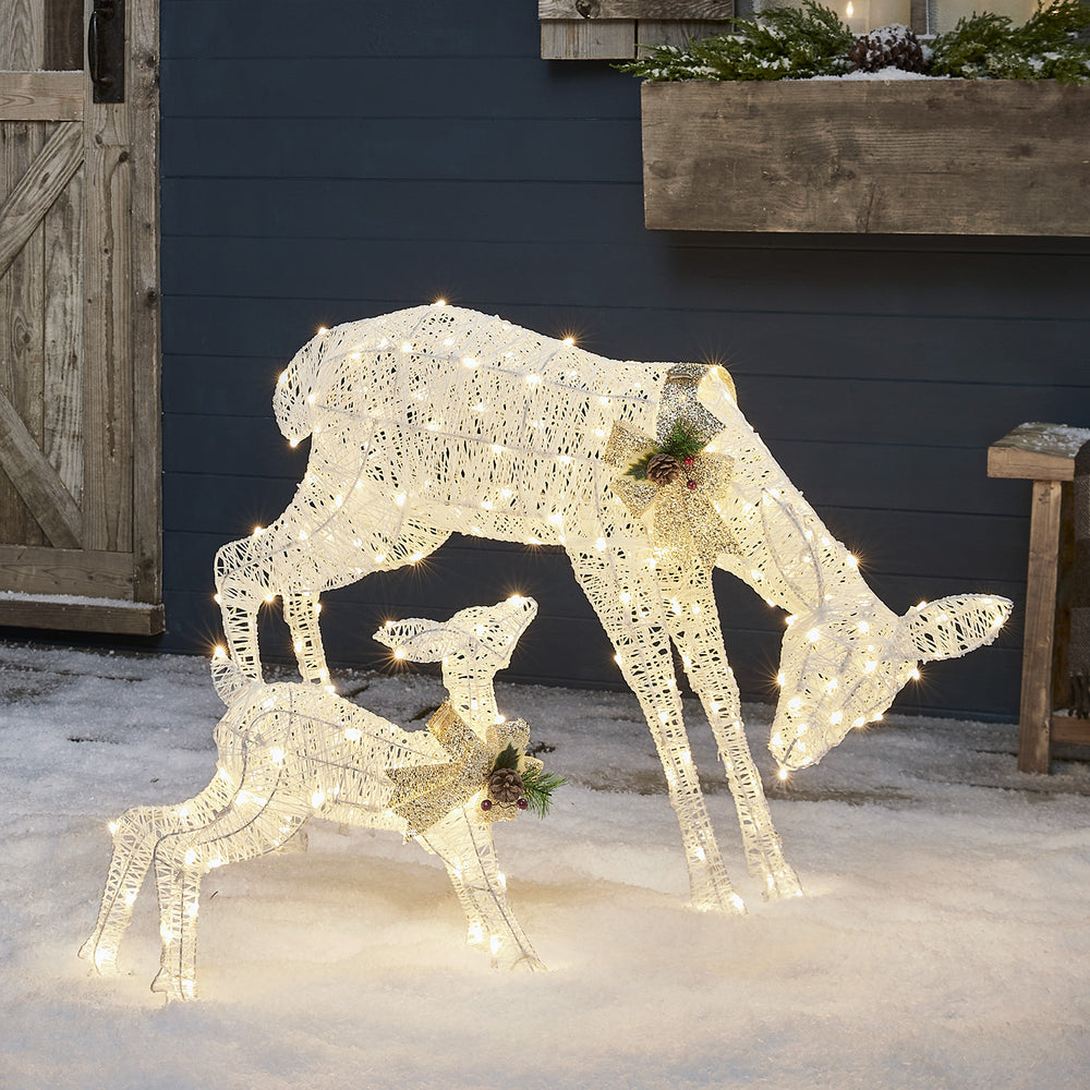 Beleuchtete weiße LED-Figuren einer Rentiermutter und ihres Kitzes mit silberner Schleife im Schnee