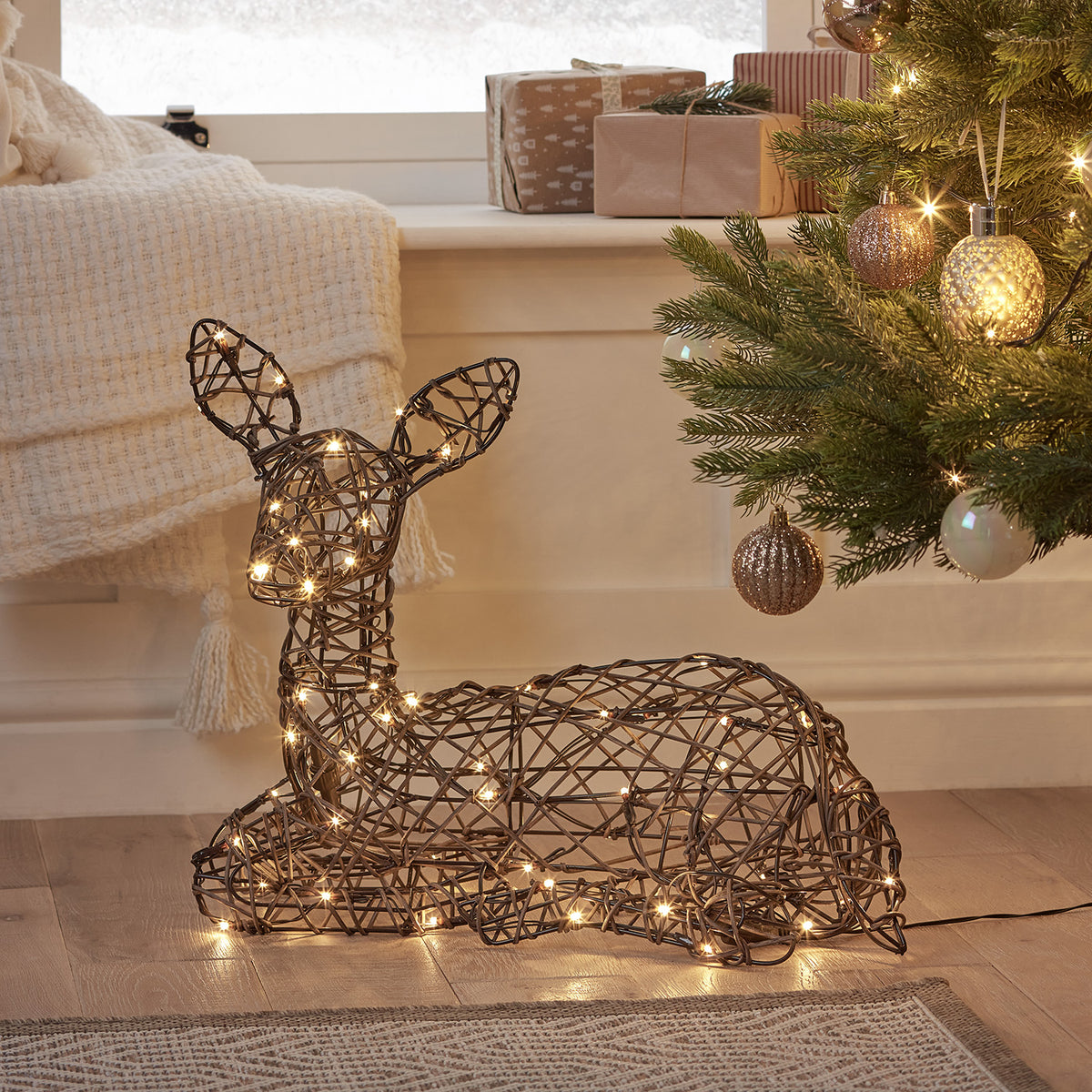 Liegendes Solar-LED-Rehkitz in Rattan-Optik neben Weihnachtsbaum und Geschenken im Wohnzimmer