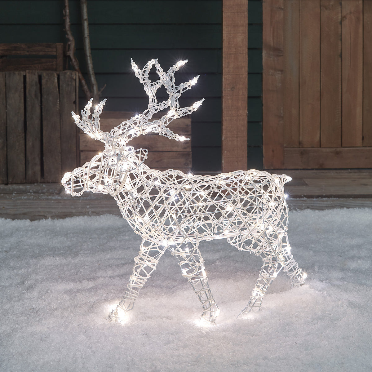 Weißes Solar-LED-Rentier in Rattan-Optik mit gemischten Bicolor-LEDs im Schnee vor Holzwand