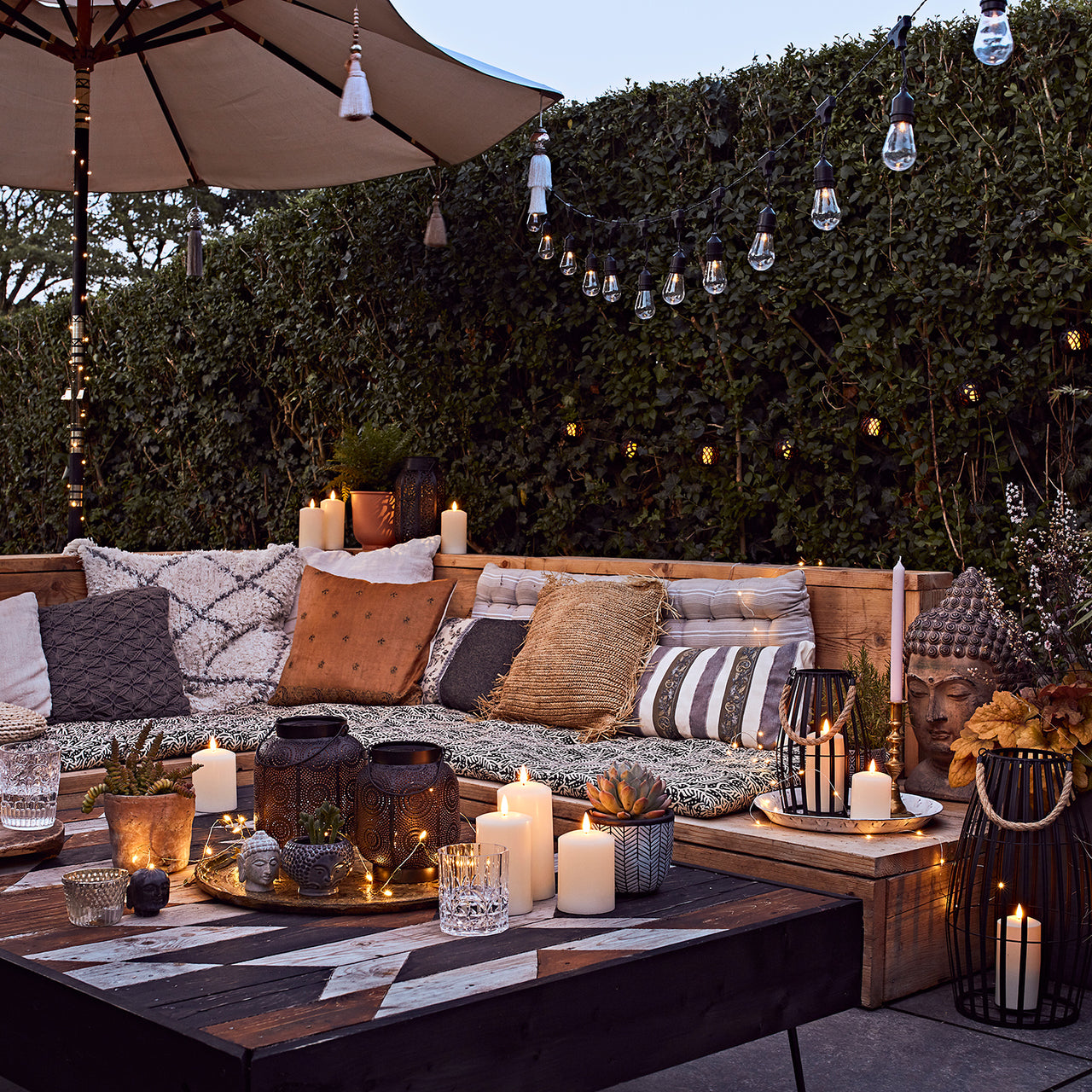 Beleuchtete Terrasse bei Dämmerung mit LED Kerzen, Sitzbank und beleuchtetem Sonnenschirm.