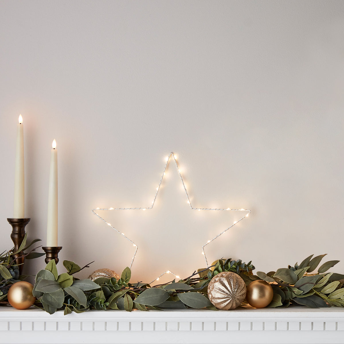 Leuchtender LED-Stern auf Kaminsims mit Kerzen, Kugeln und grüner Weihnachtsdeko