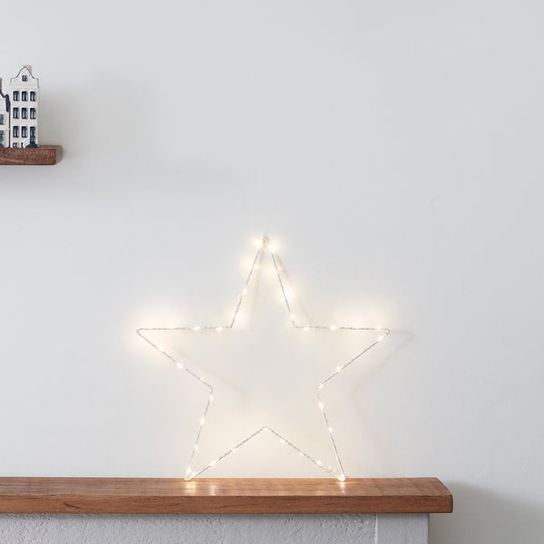 Kleiner beleuchteter LED-Stern an weißer Wand auf Holzablage