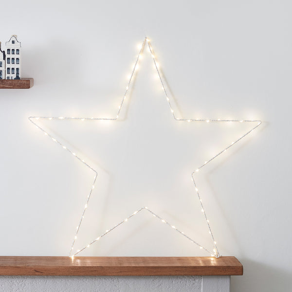 Großer beleuchteter LED-Stern an weißer Wand auf Holzablage