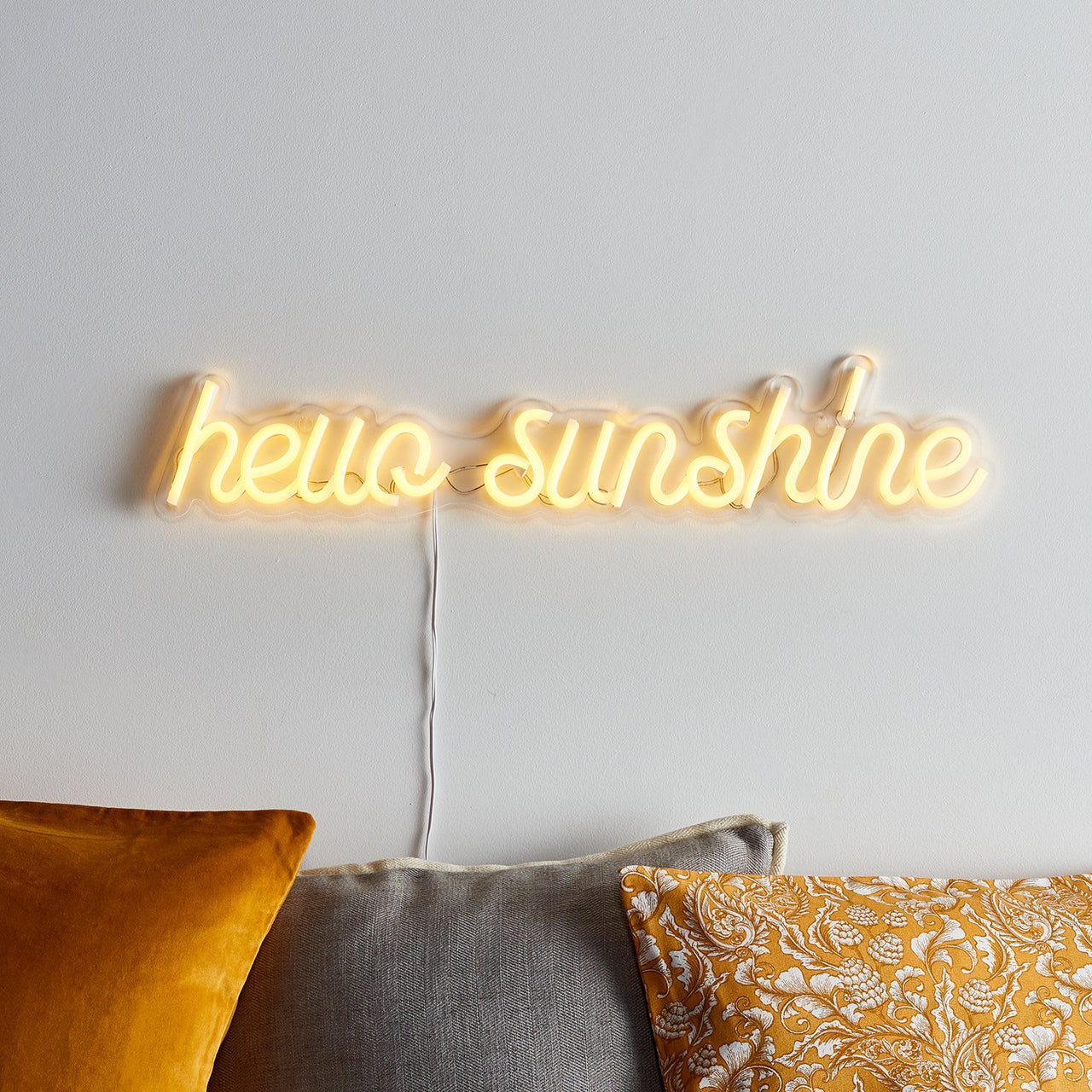 Gelbe Neonschrift hello sunshine an weißer Wand mit Kabel und Kissen.