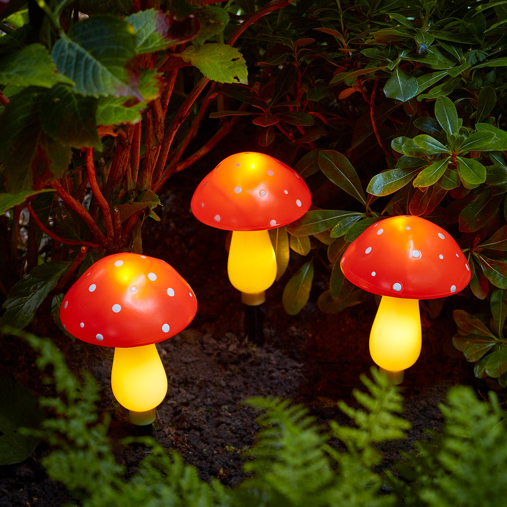 Drei Fliegenpilz Stableuchten in Rot und Gelb mit warmweißem Licht vor grünen Blättern.
