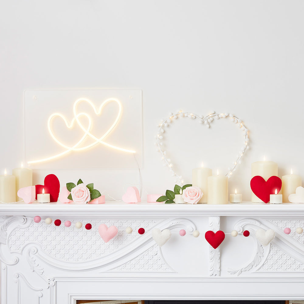 Dekorierter Kaminsims mit Micro LED Herz, Kerzen, roten Herzen und Rosen vor weißer Wand